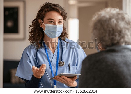 Doctor wearing safety protective mask supporting and cheering up senior patient during home visit during covid-19 pandemic. Nurse and old woman wearing facemasks during coronavirus and flu outbreak.  Royalty-Free Stock Photo #1852862014