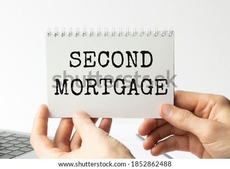 A man's hand is on the financial tables holding a business card with the inscription Second Mortgage. Business concept photo