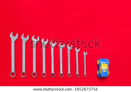 Set of wrenches different size and blue toy car lays on a red background. Banner with tools of locksmith for car service and tire fitting with industrial concept. Close-up.