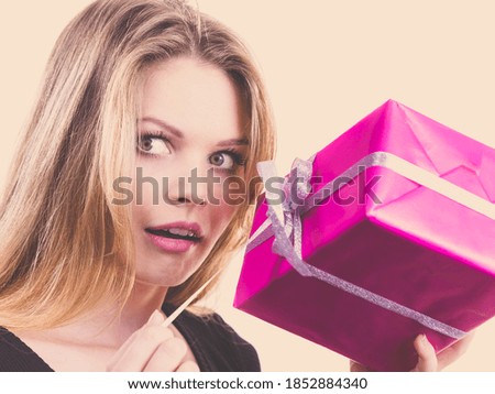 Funny cute young teenage woman being curious what is inside gift box. Female receiving present