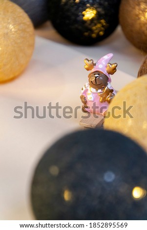 Close up picture with small figure of deer in pink costume, as Christmas wallpaper and copy space for text on the right side and lights on the back. Cartoon animal with small gifts, as decoration.