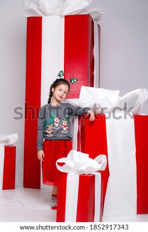 happy funny child girl in Christmas costume with big red gifts on background.