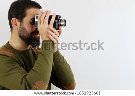 A man in a casual shirt on a white background is shooting with an 8mm camera turned sideways. Vintage concept