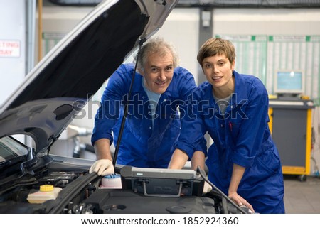 Senior mechanic and his colleague posing with a diagnostic computer placed on an open hood of a broken down car