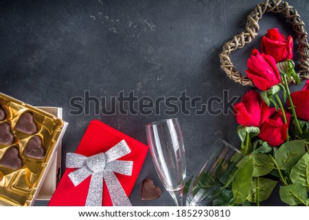 Valentine day background with Chocolates Hearts, Red Gift Box, Champagne Wine Glasses and Red Roses. Over Black Stone table Backdrop, top view