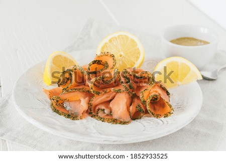 Smoked salmon rolls with lemon on white plate and mustard dip in white bowl on white wooden background