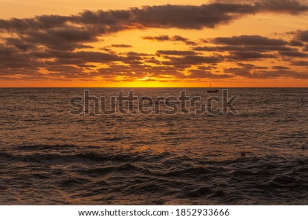 Early morning dawn, dark clouds and red glow portend a storm, a lone sailing ship is at sea