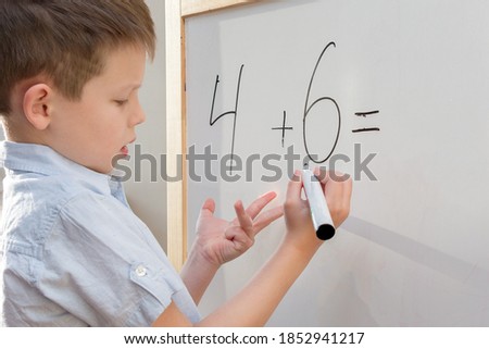A preschool-age boy with a funny facial expression stands at a white board and decides an example in mathematics. The concept is to prepare the child for school, to obtain basic knowledge and skills. Royalty-Free Stock Photo #1852941217