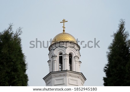 White church with a golden dome between trees against the sky
