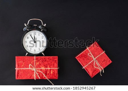 sales concept. christmas discounts.  black round clock on red giftbox, another giftbox lies near  on black background. copy space for text