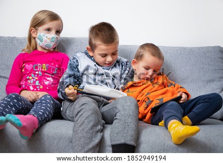 three children lie on the couch, get bored during quarantine, watch a movie on the phone