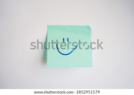 Blue sticker with happy smile drawn with blue marker in handwriting stuck on white paper background. Business note.
