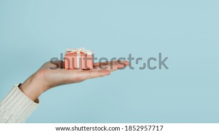 Giving Tuesday, Give, Help, Donation, Support, Volunteer concept with female hands and pink gift box on blue background. Heart shaped female fingers and pink gift box close up