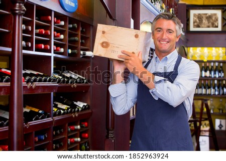 Smiling worker holding a box of new wine stock in a wine shop