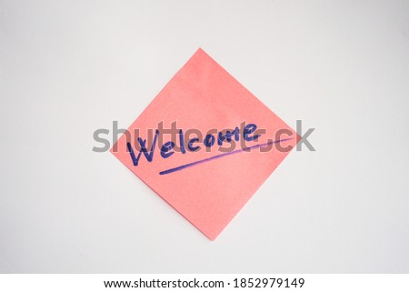 Pink sticker with word WELCOME drawn red marker in handwriting stuck on white paper background. Business note. Greeting.