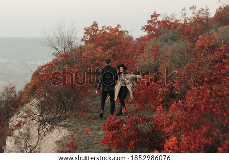 Happy stylish woman holding man by the hand and walking down the autumn mountain valley looks and smiles at her man.
