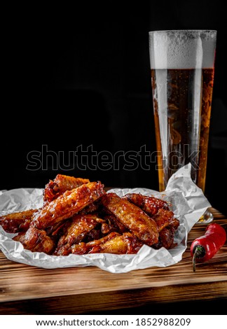 glass of fresh beer and fried chicken wings on wooden table on black background
