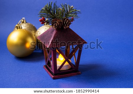 Christmas decorations: burning lantern and golden Christmas balls on a dark blue background. Selective focus.