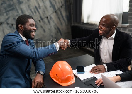 Two African Americans signed a cooperation agreement. Business investors shake hands. Orange construction hard hat on office desk
