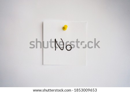 White note paper with negative answer NO written in black handwriting pinned on white paper background with yellow pin. Business note.