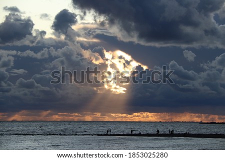 Dark clouds with rays in the center against the background of a sunset over the sea. black silhouettes of people