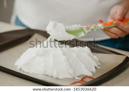 А photo of the hands of a young woman who is creating with a scapula a form of a giant meringue on a tray. A girl is preparing to cook a delicious lemon meringue tart.