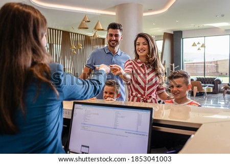 Smiling family of four in the hotel lobby check in at the reception for vacation. Royalty-Free Stock Photo #1853041003