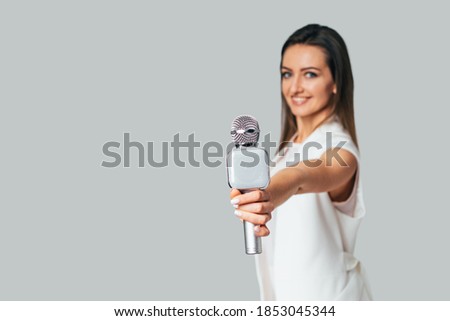 Host of events showing microphone to the camera. Light gray background. Closeup.