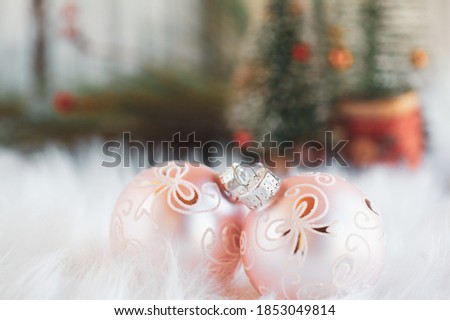 Two pink Christmas ornaments lying on a white rug. Selective focus with Christmas trees blurred into the background.