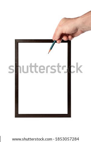 Hand holding a pencil. Wooden frame on white isolated background. White sheet inside the frame. Place to place information. Empty space for insertion. The pencil points to the sheet.