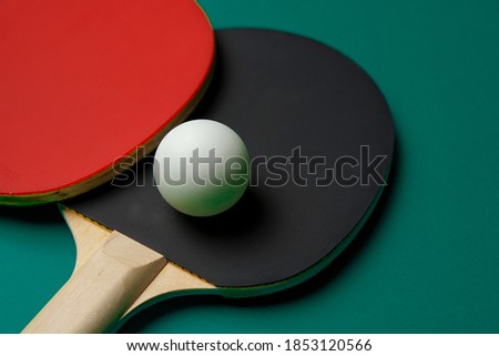 Two table tennis or ping pong rackets and ball on the dark green table.