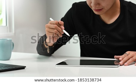 Cropped shot of graphic designer or photographer hand holding stylus pen drawing on the graphic tablet.