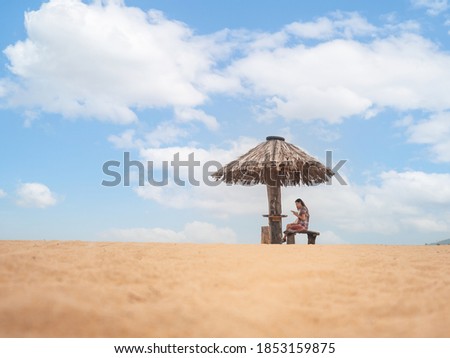 Asian woman sitting under straw umbrella on seashore. female using mobile smart phone on beach. copy space provided.