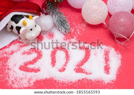 Decorations for the new year, postcard design. Toy bull in a santa hat, new year garland, inscription 2021 on the snow.