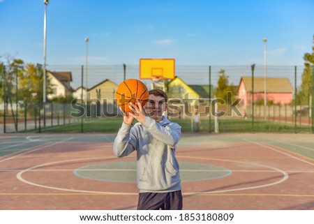 The guy is holding a basketball in his hands and is going to throw it into the hoop on the playground