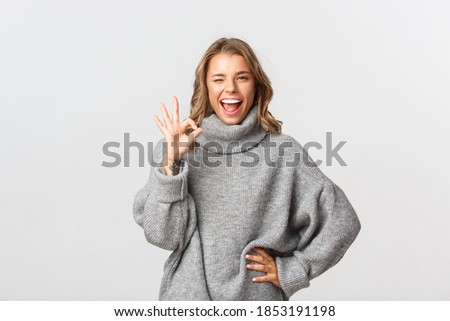 Confident smiling woman showing no problem gesture, make okay sign and winking self-assured, standing over white background