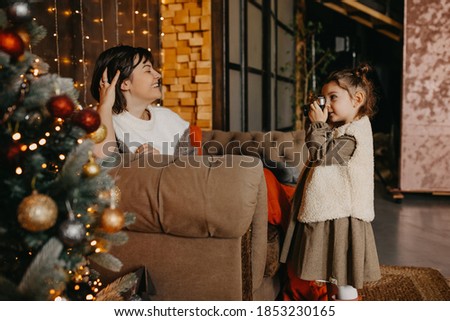 Little girl taking pictures of her mother at home, next to a christmas tree.