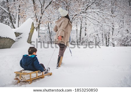 Mom pulling her son on the sled. Winter time, outdoor activities