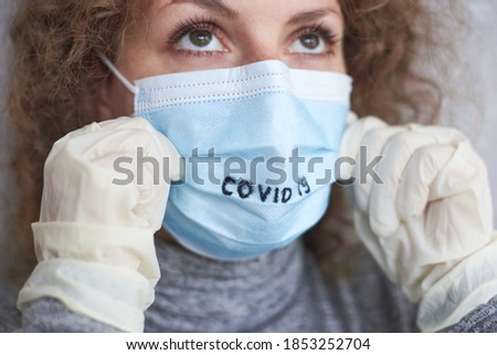 A woman's hands in medical gloves hold a mask with the inscription Covid 19, the theme of protection against coronavirus.