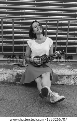 Black and white shot of Young beautiful woman with ukulele having fun at the background