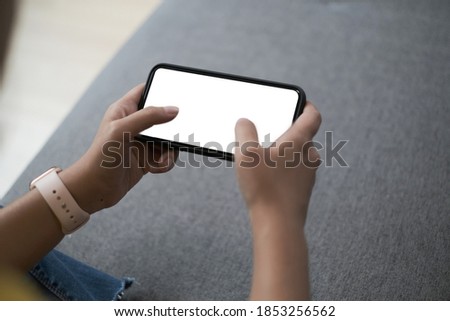 Mockup image of woman is using a black mobile phone with blank screen horizontally for watching at home. 