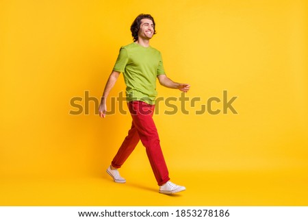 Full length body size photo of man hurrying up stepping forward smiling in red trousers isolated on vibrant yellow color background