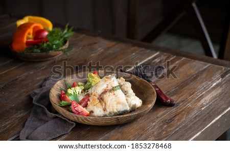Fried fish fillet with vegetable salad on a wooden table