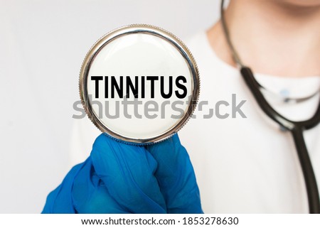 The doctor's blue - gloved hands show the word TINNITUS- . a gloved hand on a white background. Medical concept. the medicine
