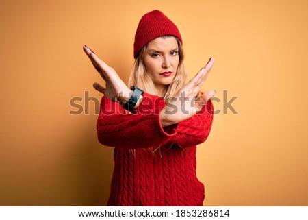 Young beautiful blonde woman wearing casual sweater and wool cap over white background Rejection expression crossing arms and palms doing negative sign, angry face