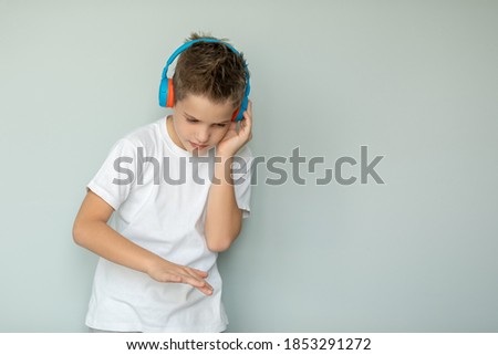 A boy in a white T-shirt listens to his favorite music with headphones. The teenager moves in a dance to the beat of the music, isolated on a gray background. Large portrait.
