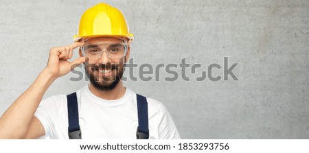 profession, construction and building concept - happy smiling male worker or builder in yellow helmet and overall over grey concrete background