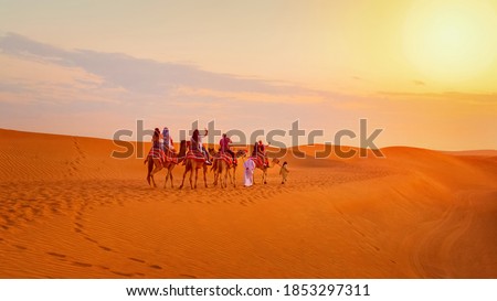 Caravan with group of tourists riding camels through Dubai desert during safari adventure – People exploring sand dunes at sunset in UAE Royalty-Free Stock Photo #1853297311