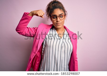 Beautiful african american businesswoman wearing jacket and glasses over pink background Strong person showing arm muscle, confident and proud of power