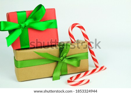 Gifts wrapped with brown and red paper and green bows next to Christmas decoration on white background